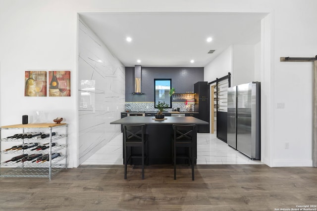 kitchen featuring a kitchen island, wall chimney range hood, stainless steel fridge, a breakfast bar, and light wood-type flooring