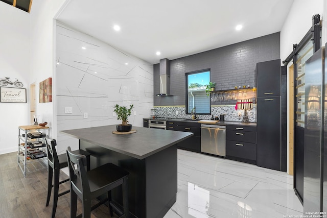 kitchen featuring dishwasher, a kitchen island, wall chimney exhaust hood, a breakfast bar area, and light wood-type flooring