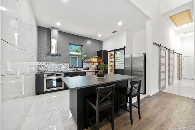 kitchen featuring a kitchen island, a breakfast bar, a barn door, light hardwood / wood-style flooring, and stainless steel appliances