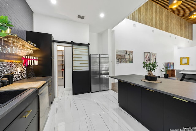 kitchen featuring a high ceiling, a barn door, stainless steel appliances, and backsplash