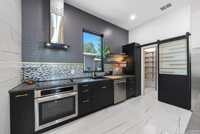 kitchen with sink, a barn door, stainless steel appliances, wall chimney exhaust hood, and decorative backsplash