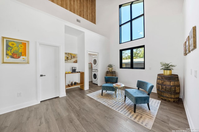 living area featuring stacked washer / drying machine, a towering ceiling, and light hardwood / wood-style flooring