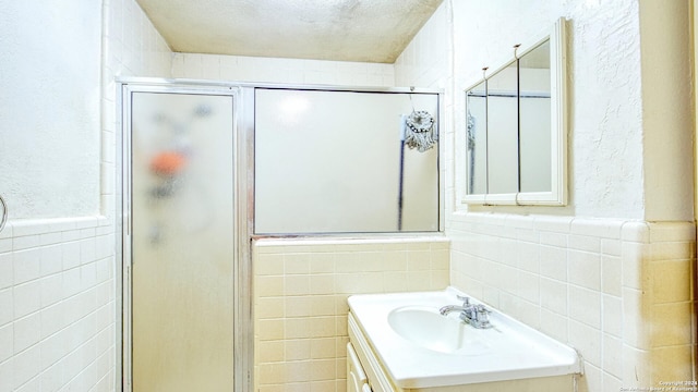 bathroom with vanity, a textured ceiling, tile walls, and a shower with shower door