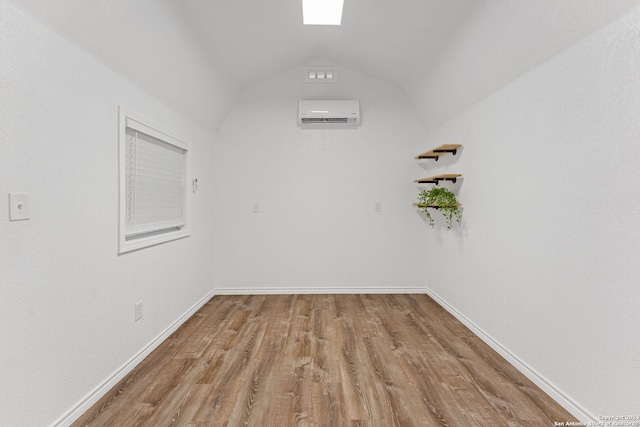 spare room featuring light hardwood / wood-style floors, lofted ceiling, and an AC wall unit