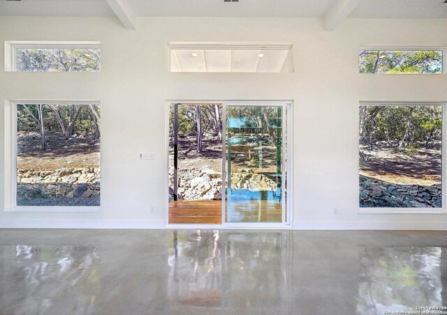 interior space featuring concrete flooring, beam ceiling, and baseboards