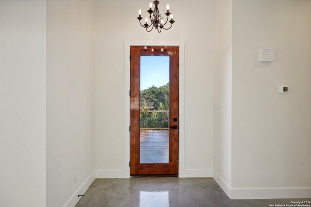 doorway featuring concrete flooring, a notable chandelier, and baseboards