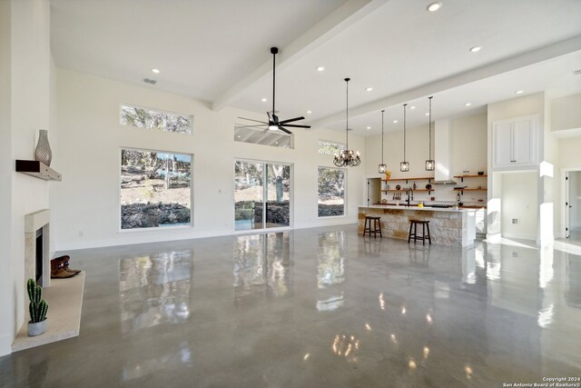 living room with sink, beamed ceiling, a fireplace, ceiling fan with notable chandelier, and a high ceiling