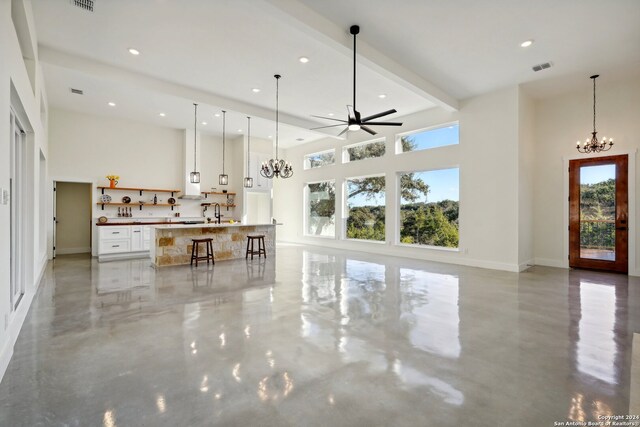 unfurnished living room featuring beam ceiling, ceiling fan with notable chandelier, and a high ceiling