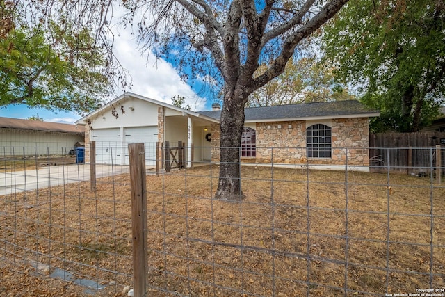 ranch-style house featuring an attached garage, a fenced front yard, driveway, and stone siding