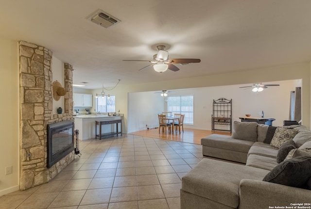 living room with a stone fireplace, light tile patterned flooring, and ceiling fan