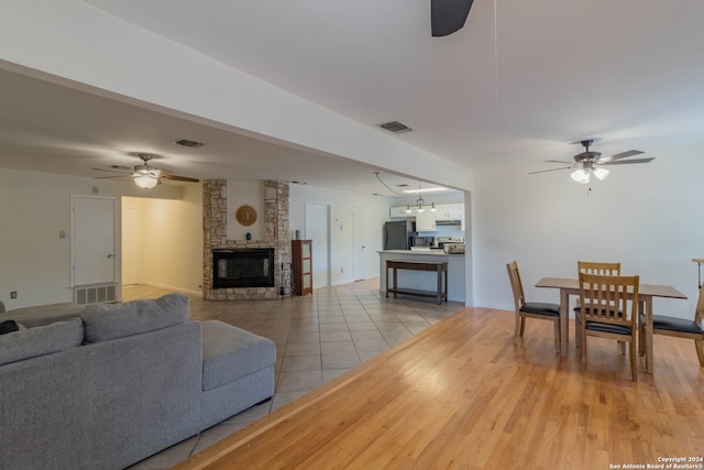 living room featuring ceiling fan, a stone fireplace, and light wood-type flooring