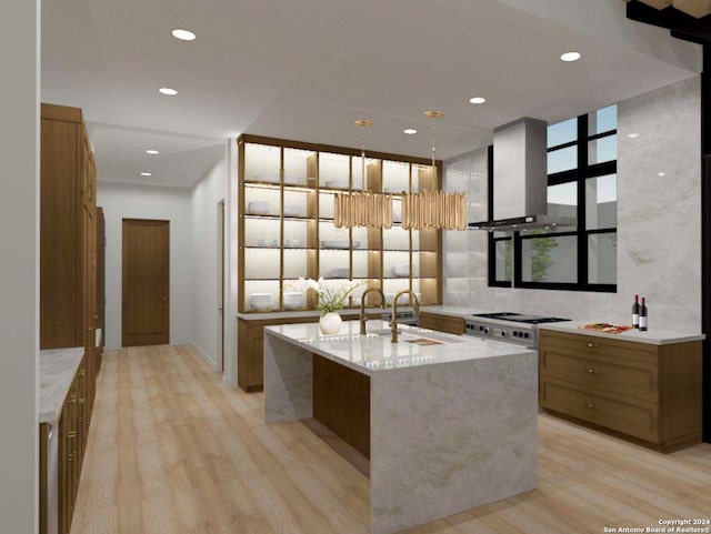 kitchen featuring light hardwood / wood-style floors, extractor fan, light stone counters, an island with sink, and pendant lighting