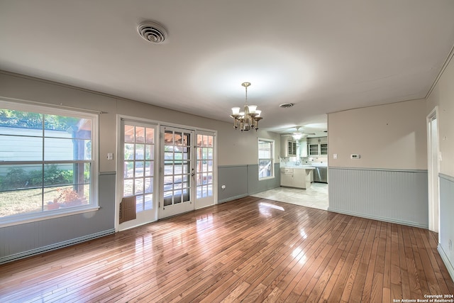 unfurnished living room featuring a wealth of natural light, light hardwood / wood-style floors, and ceiling fan with notable chandelier