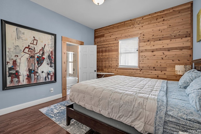 bedroom featuring ensuite bath, wooden walls, and dark hardwood / wood-style floors