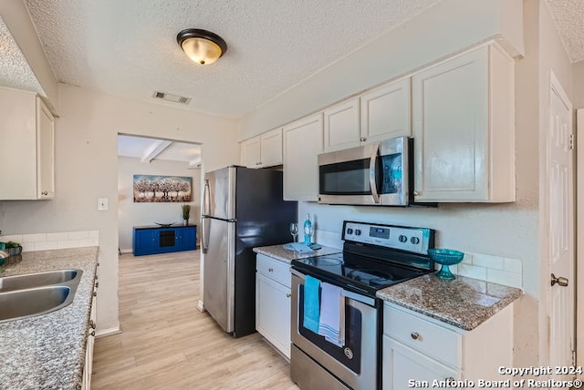 kitchen featuring appliances with stainless steel finishes, light wood-type flooring, a textured ceiling, white cabinetry, and light stone counters