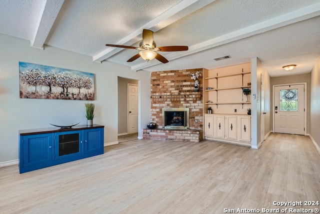 unfurnished living room featuring a fireplace, a textured ceiling, light hardwood / wood-style floors, ceiling fan, and beam ceiling