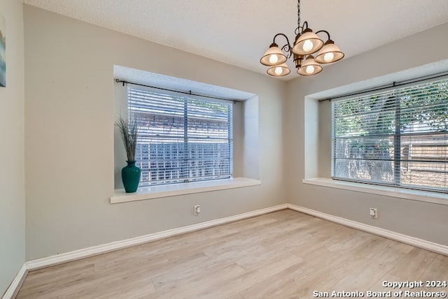 empty room with a notable chandelier and light hardwood / wood-style floors