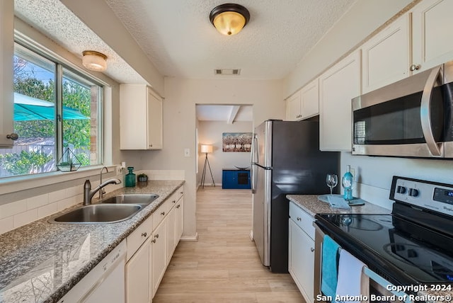 kitchen with light hardwood / wood-style flooring, stainless steel appliances, sink, light stone countertops, and white cabinets