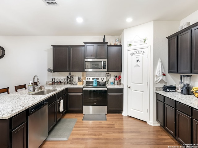 kitchen with a kitchen breakfast bar, kitchen peninsula, stainless steel appliances, sink, and light hardwood / wood-style floors