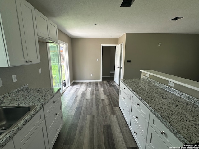 kitchen featuring light stone countertops, sink, a textured ceiling, white cabinetry, and dark hardwood / wood-style floors