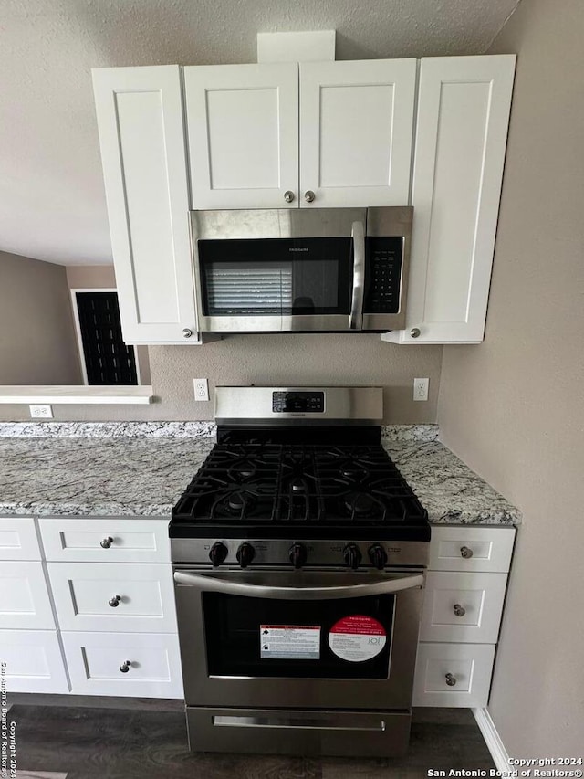 kitchen featuring appliances with stainless steel finishes, white cabinets, light stone counters, and dark hardwood / wood-style floors