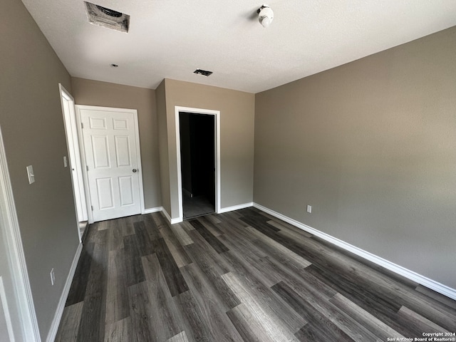 unfurnished bedroom with a closet, a textured ceiling, and dark hardwood / wood-style floors