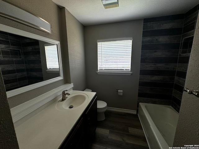 full bathroom with hardwood / wood-style floors, a textured ceiling, toilet, vanity, and tiled shower / bath combo