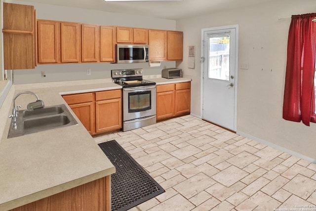 kitchen featuring appliances with stainless steel finishes, a sink, open shelves, light countertops, and baseboards