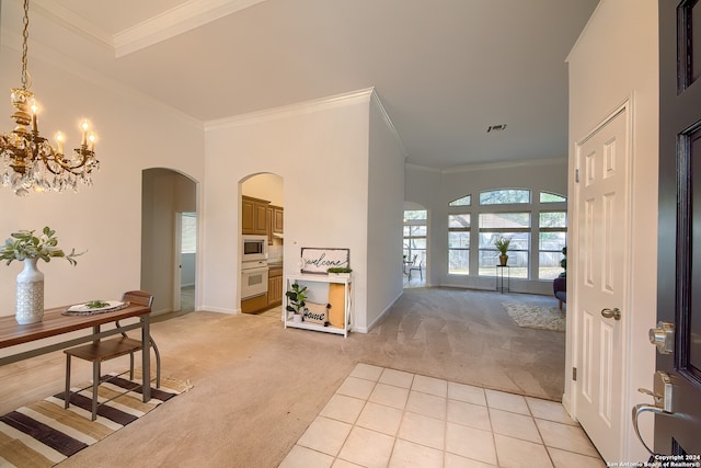 foyer entrance featuring a high ceiling, crown molding, an inviting chandelier, and light colored carpet