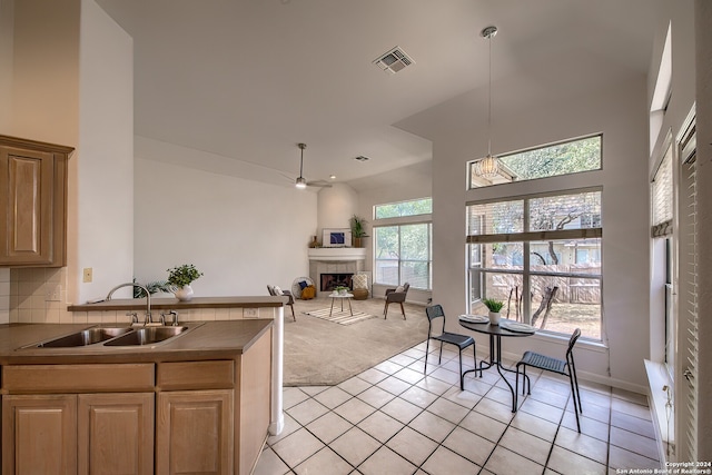 kitchen with tasteful backsplash, sink, a tiled fireplace, light carpet, and ceiling fan