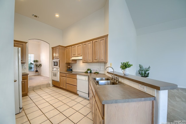 kitchen with white appliances, tasteful backsplash, sink, high vaulted ceiling, and light tile patterned floors