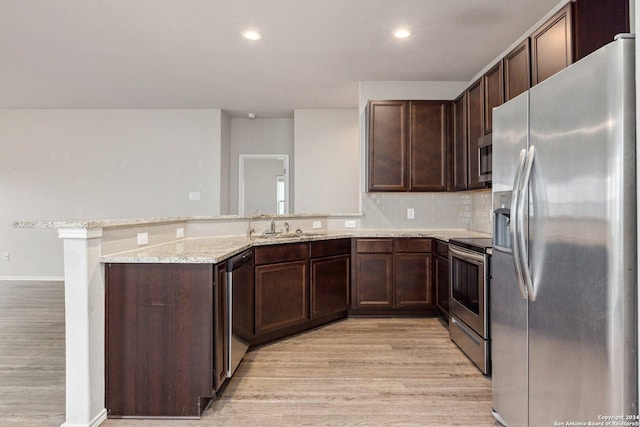 kitchen with light wood-type flooring, appliances with stainless steel finishes, dark brown cabinets, light stone counters, and kitchen peninsula