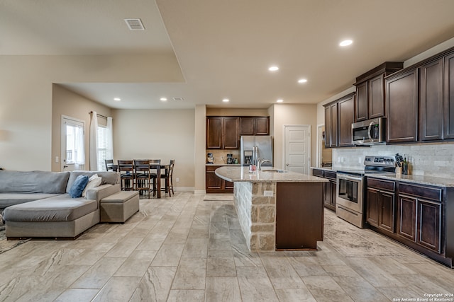 kitchen with dark brown cabinets, backsplash, an island with sink, stainless steel appliances, and sink