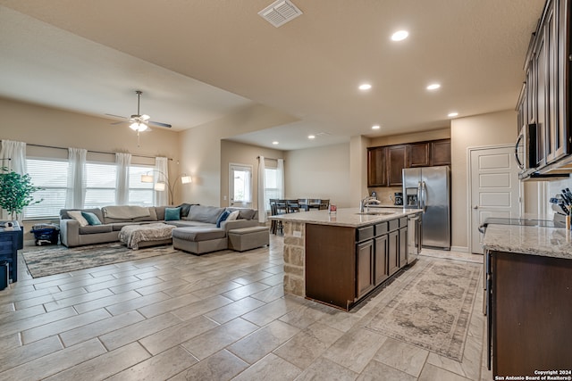 kitchen featuring a kitchen island with sink, dark brown cabinets, sink, light stone countertops, and appliances with stainless steel finishes