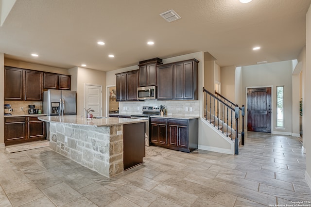 kitchen featuring sink, appliances with stainless steel finishes, backsplash, and an island with sink