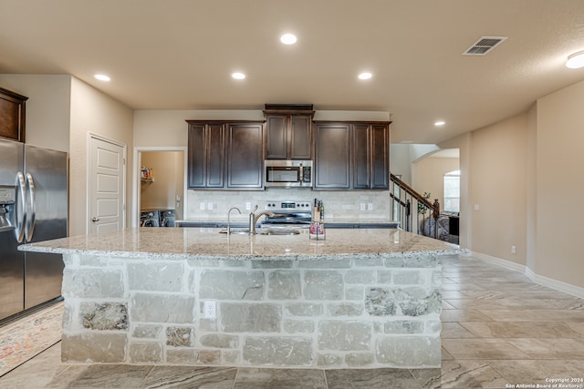 kitchen with an island with sink, light stone counters, stainless steel appliances, and tasteful backsplash