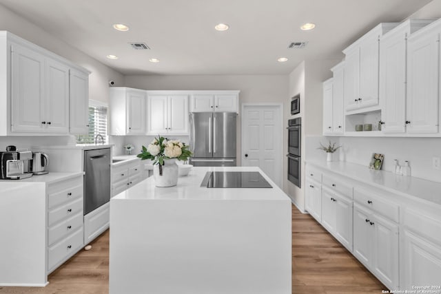 kitchen with stainless steel appliances, light wood-type flooring, a kitchen island, and white cabinets