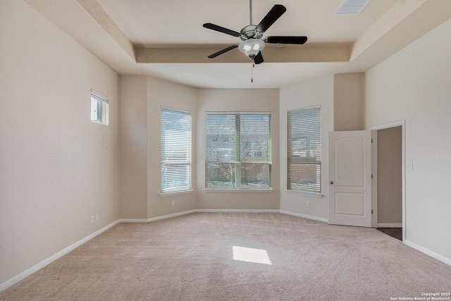 empty room with carpet floors, a raised ceiling, ceiling fan, and visible vents