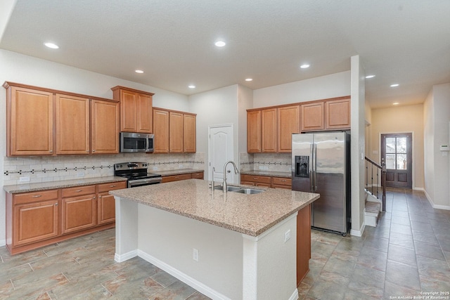 kitchen featuring a kitchen island with sink, light stone countertops, a sink, backsplash, and stainless steel appliances