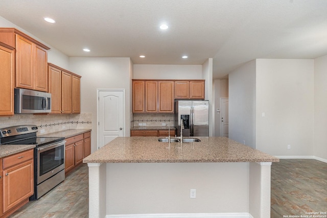 kitchen with a kitchen island with sink, light stone countertops, tasteful backsplash, a sink, and appliances with stainless steel finishes