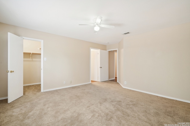 unfurnished bedroom featuring a spacious closet, ceiling fan, a closet, and light colored carpet