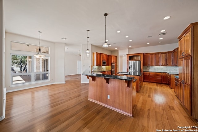 kitchen with backsplash, a kitchen breakfast bar, stainless steel appliances, and light hardwood / wood-style floors