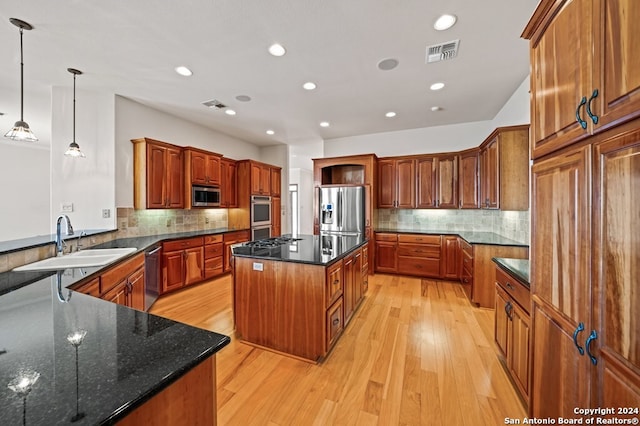 kitchen featuring appliances with stainless steel finishes, sink, light wood-type flooring, a center island, and hanging light fixtures