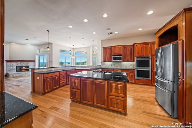 kitchen with a kitchen island, hanging light fixtures, a brick fireplace, light wood-type flooring, and appliances with stainless steel finishes