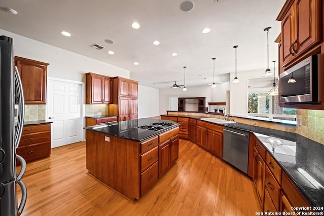 kitchen with stainless steel appliances, sink, a center island, decorative light fixtures, and light hardwood / wood-style floors