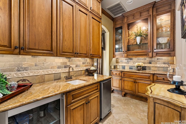 kitchen with light stone counters, wine cooler, a sink, visible vents, and brown cabinetry