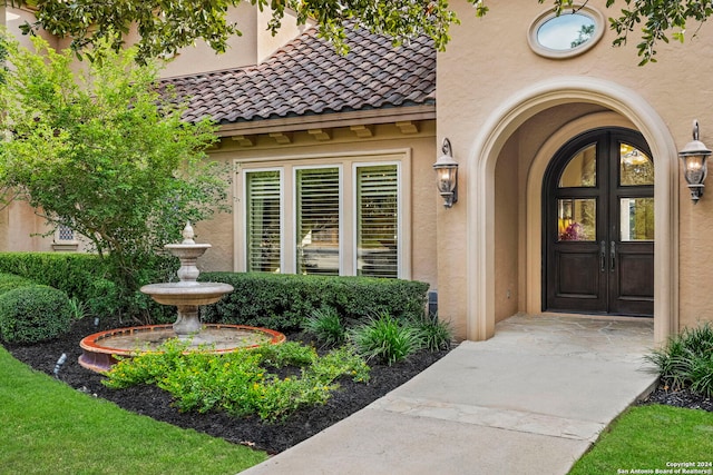 view of exterior entry featuring french doors, a tile roof, and stucco siding