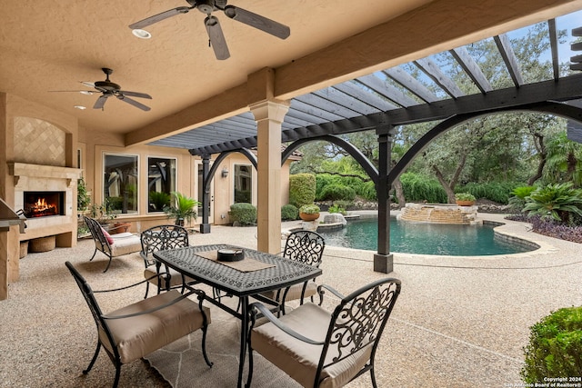 view of patio / terrace with a warm lit fireplace, a ceiling fan, a pool with connected hot tub, a pergola, and outdoor dining space