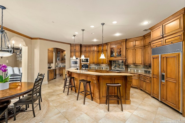 kitchen featuring built in appliances, arched walkways, a kitchen breakfast bar, backsplash, and brown cabinetry