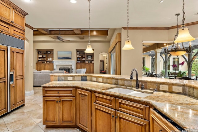 kitchen featuring a warm lit fireplace, brown cabinetry, ceiling fan, light stone countertops, and a sink